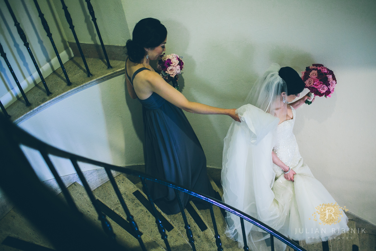 Bridesmaid holds the gown as the bride walks down the stairs