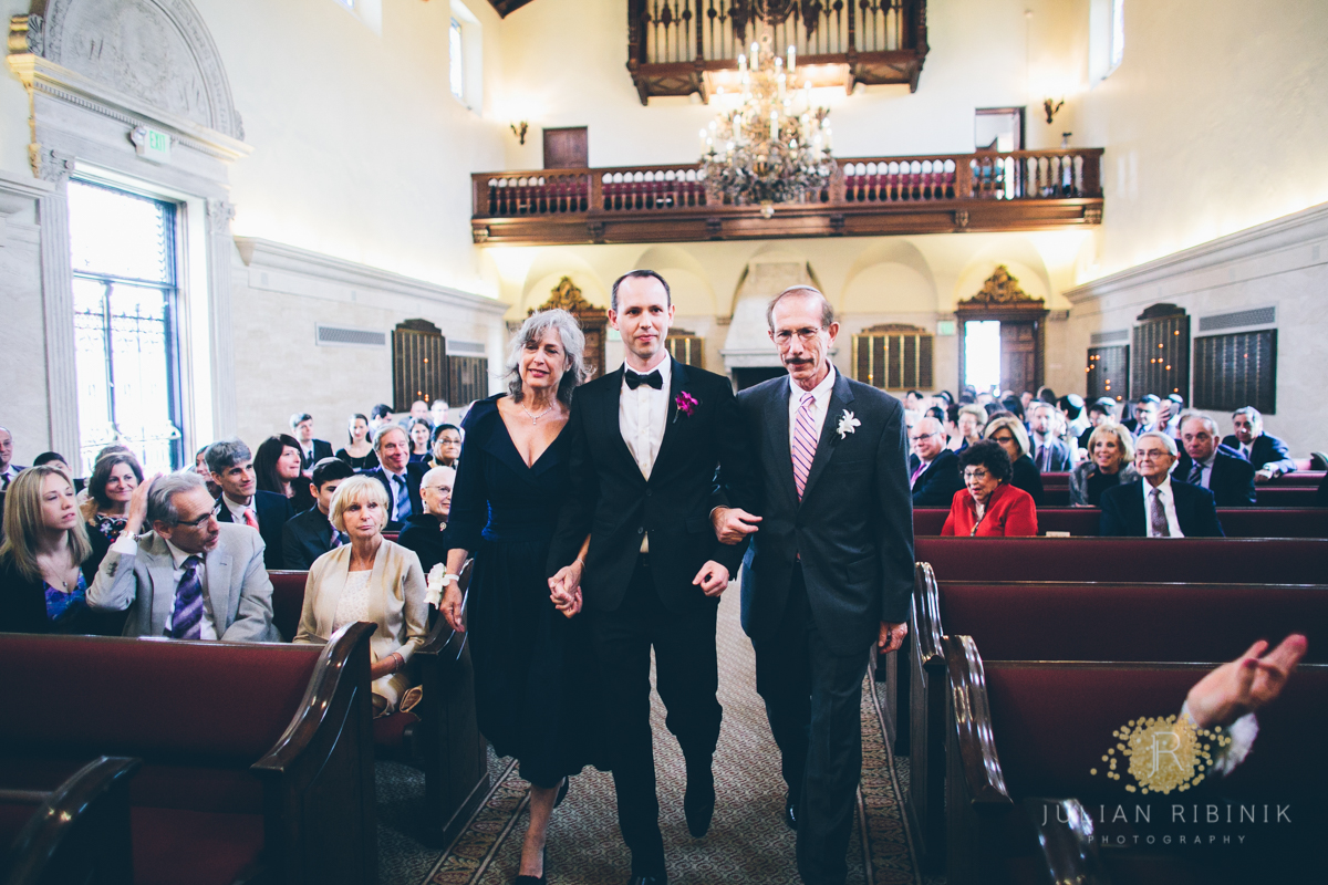 The groom along with his parents walking down the aisle