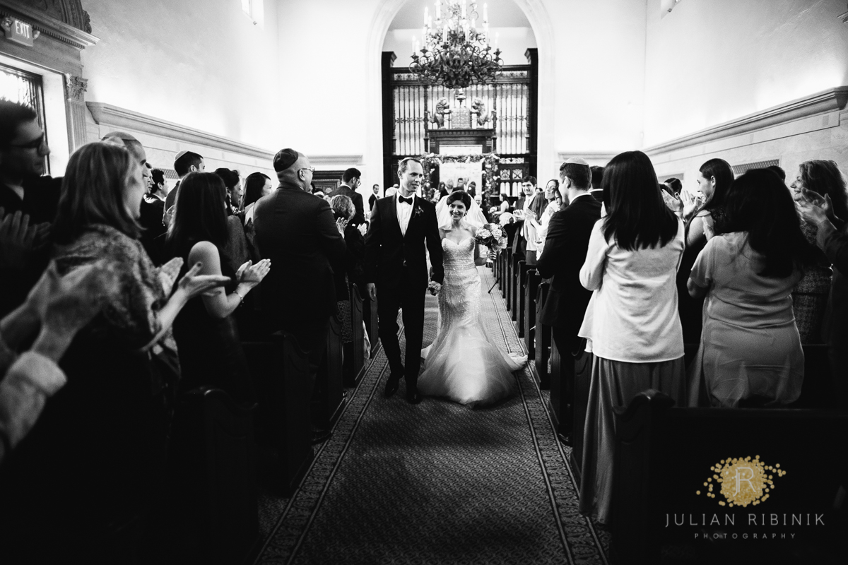 A black and white photo of bride and groom walking down the aisle