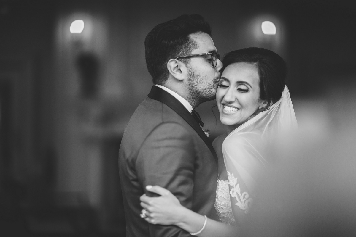 A black and white photo of the groom kissing his bride