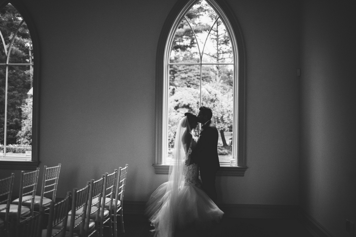 The bride and groom share a kiss in front of a beautiful window