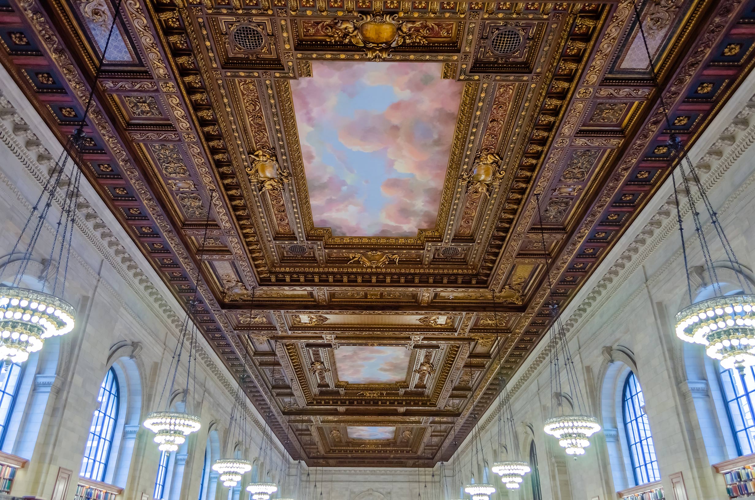 Ornate painted ceiling, chandeliers, marble walls, and tall windows inside the New York Public Library