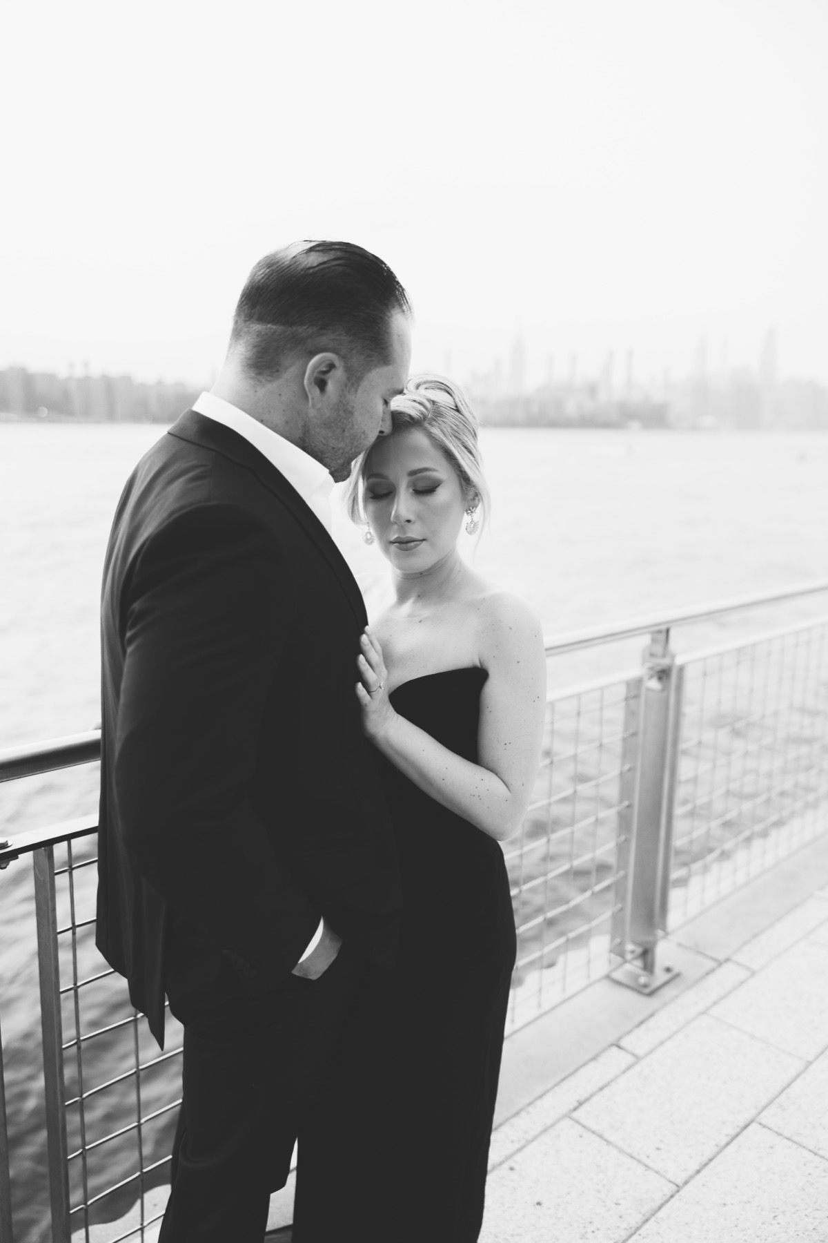 Black-and-white engagement portrait beside the East River with the Manhattan skyline in the distance