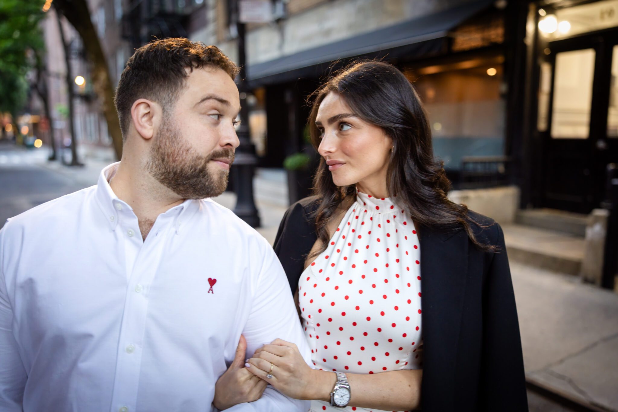 Couple walking arm in arm past softly lit West Village storefronts in the evening