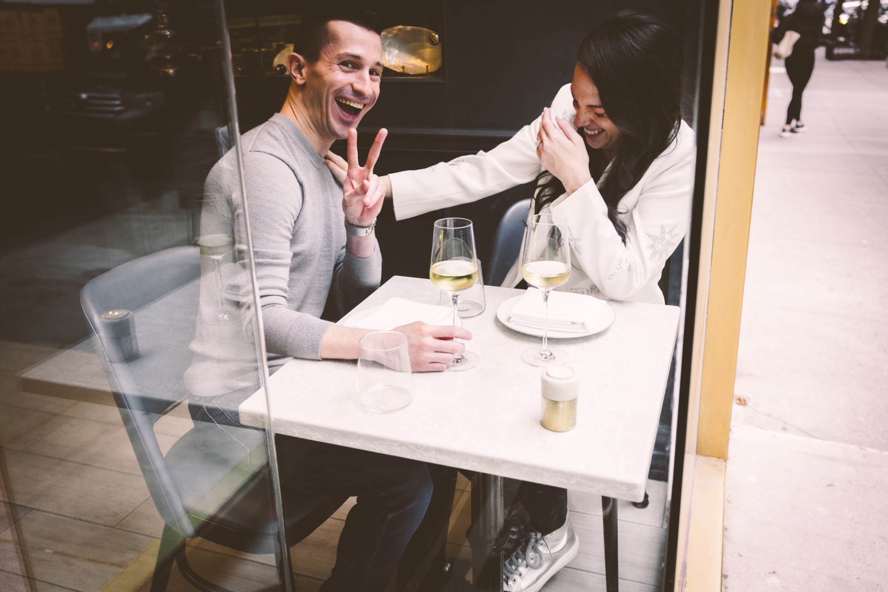 Couple laughing together beside a restaurant window on the Upper East Side.