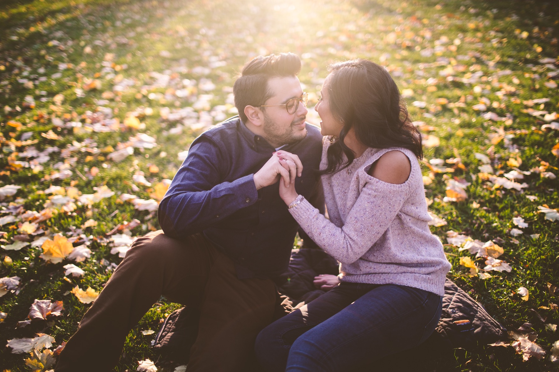 Couple seated together among autumn leaves during a Central Park engagement session