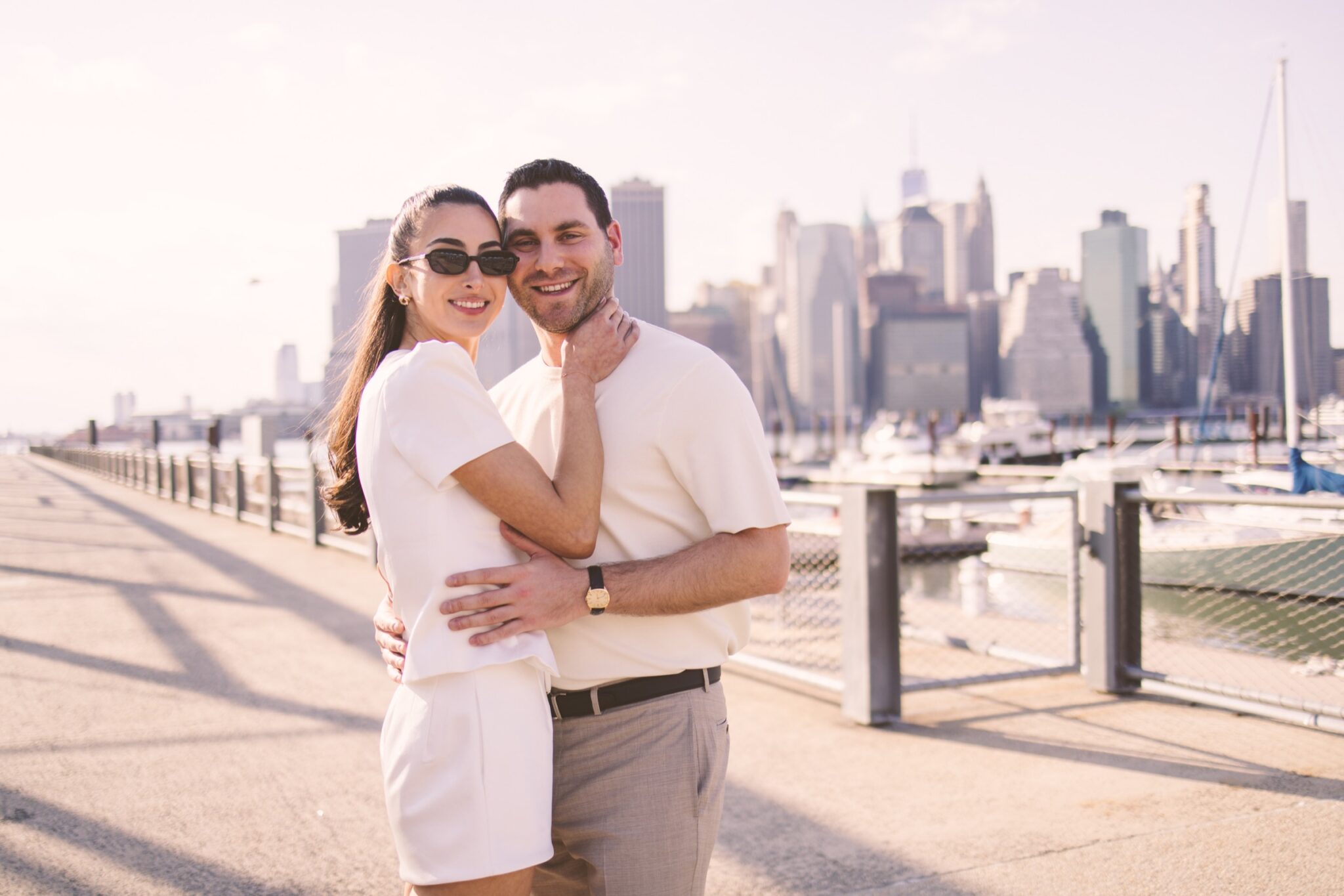 Couple embracing along the Brooklyn waterfront with the Lower Manhattan skyline behind them