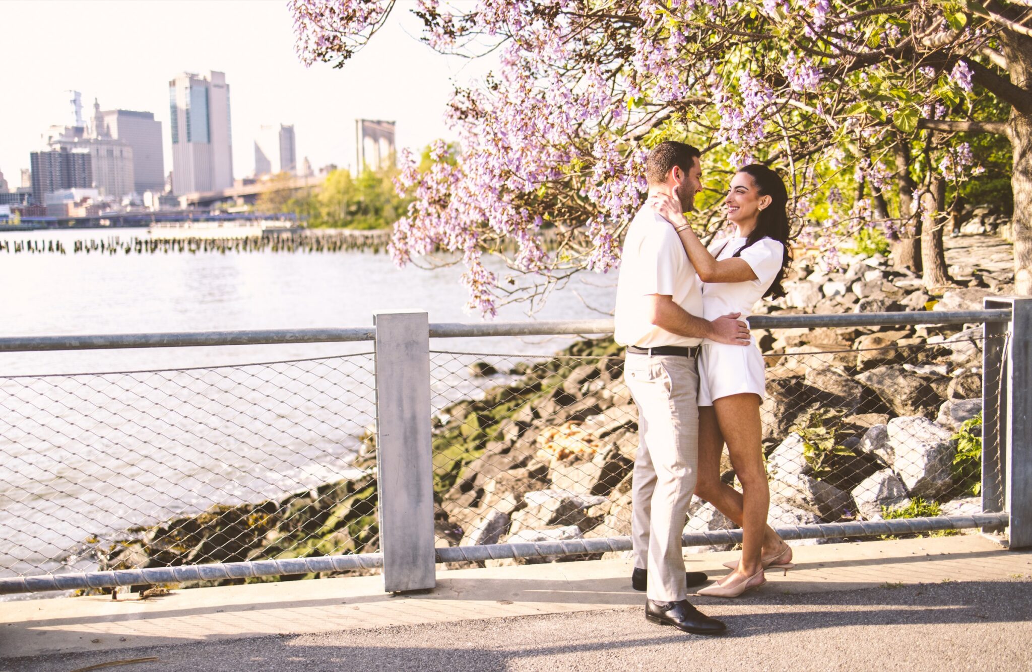 Couple embracing beneath spring blossoms beside the East River in Brooklyn Bridge Park