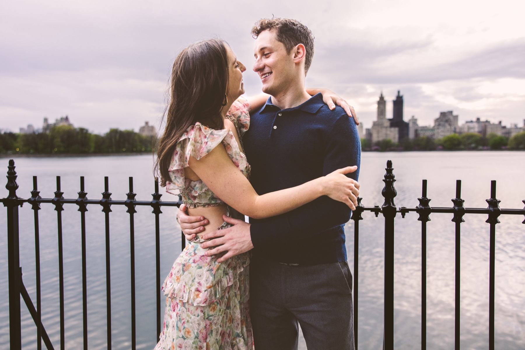 Couple embracing beside the Jacqueline Kennedy Onassis Reservoir with the Upper West Side skyline behind them