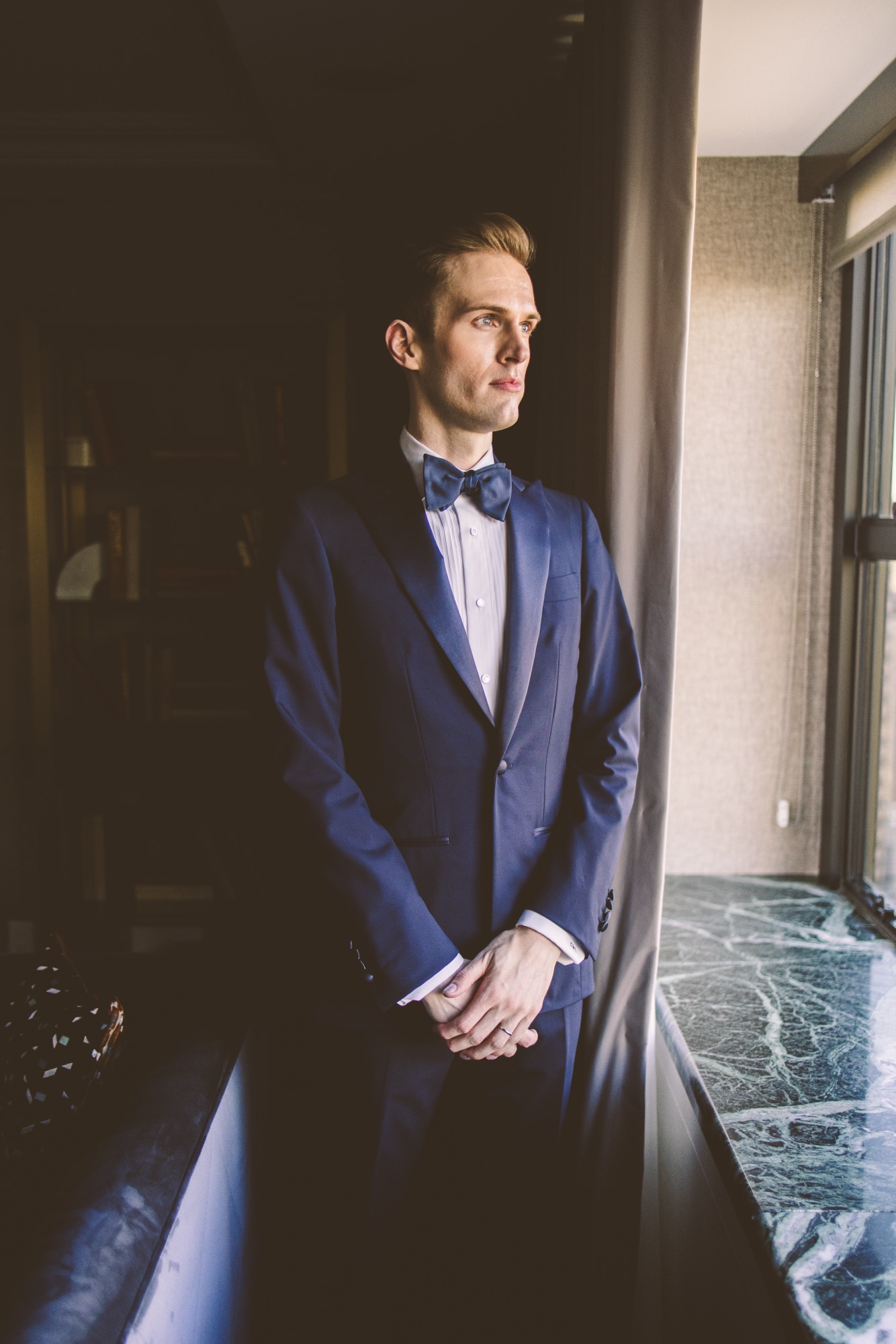 Portrait in a midnight blue tuxedo beside a window in the hotel suite