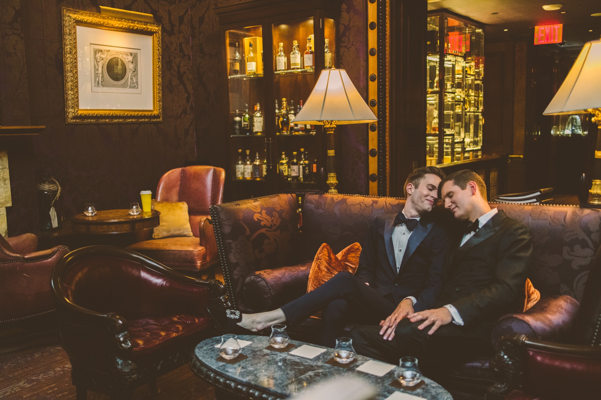 A couple on a leather sofa in a club room lit by table lamps