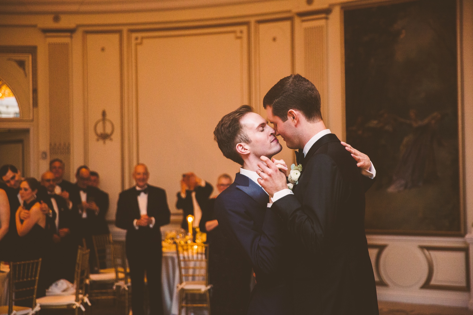A couple kissing at the reception as seated guests look on