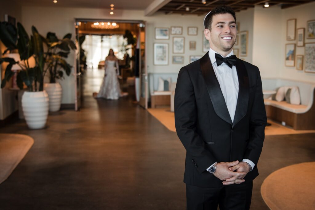 The groom waiting with his back turned at the far end of the hotel lobby before the first look