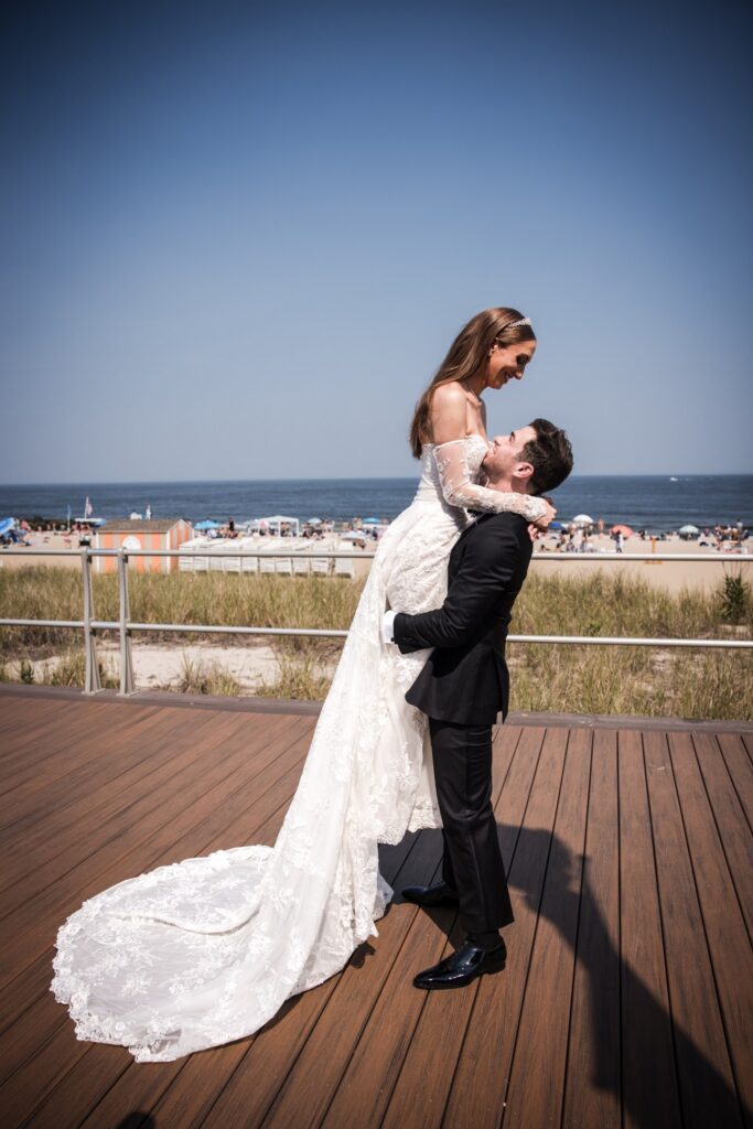 The groom lifting the bride on the boardwalk, her veil taken by the wind