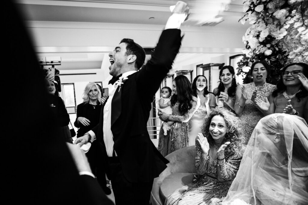 The groom with one arm raised after the veiling, the room celebrating around him