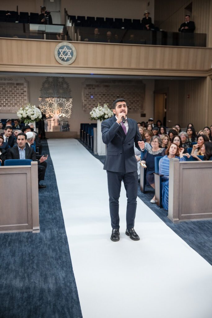 The cantor singing down the white aisle runner in the sanctuary at Ohel Yaacob