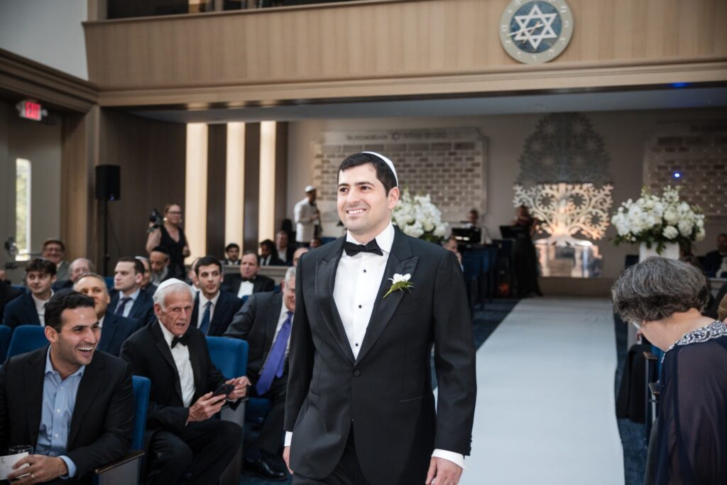 The groom walking alone down the aisle toward the chuppah
