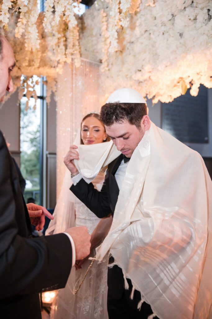 The groom's tallit being drawn up over his head during the ceremony, the Sephardic form