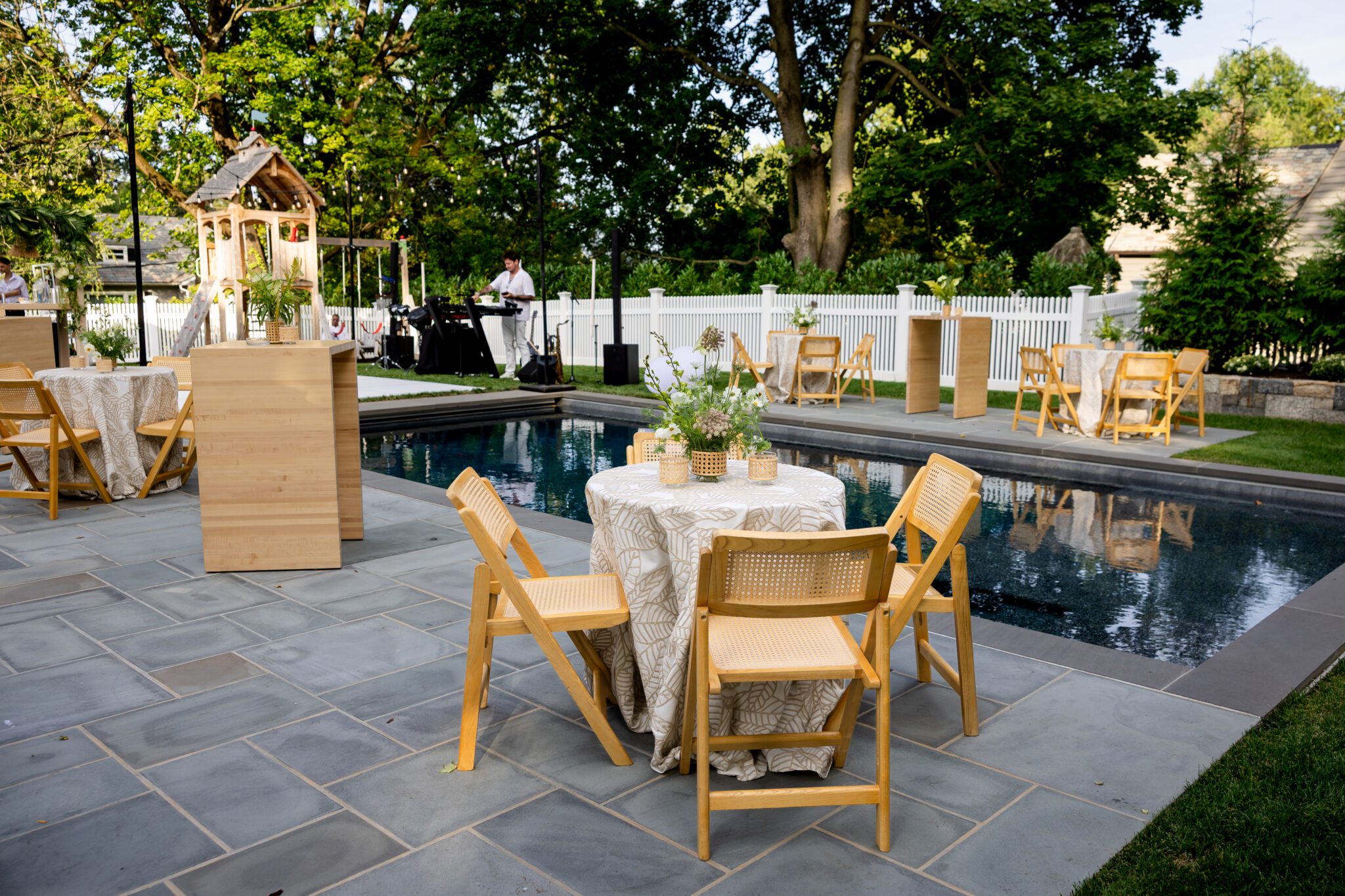 Poolside cocktail tables with woven chairs and white florals before a Greenwich birthday party