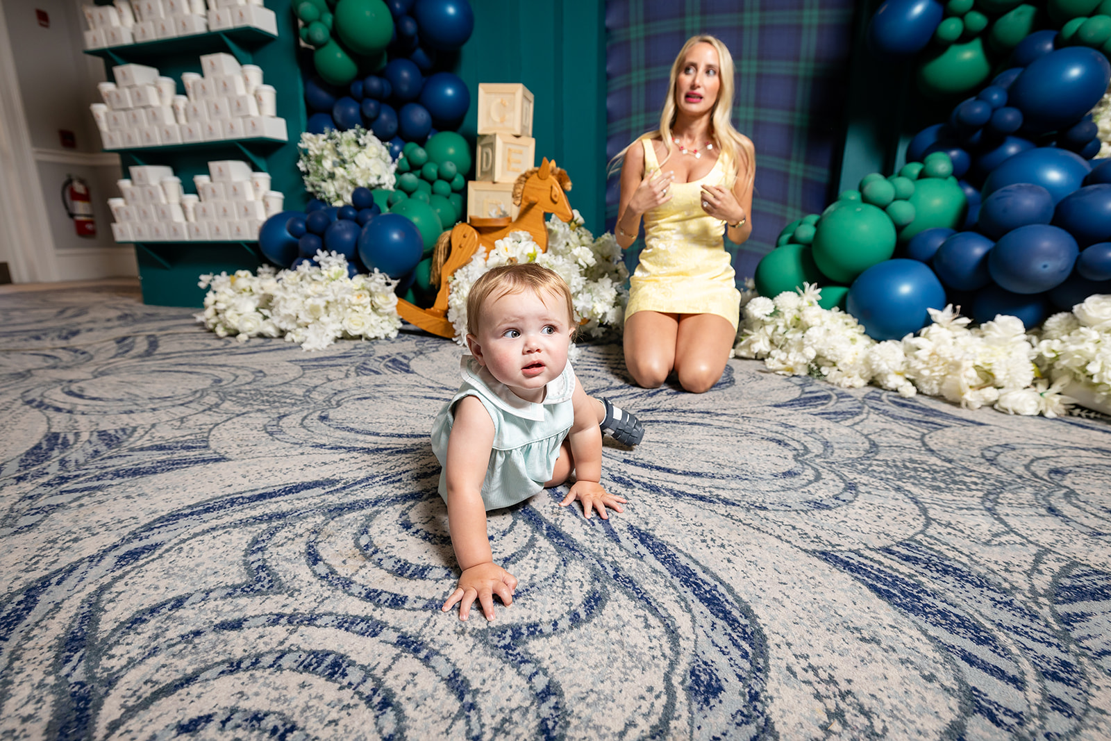 Theo with family beneath a blue and green balloon installation at a teddy bear first birthday party